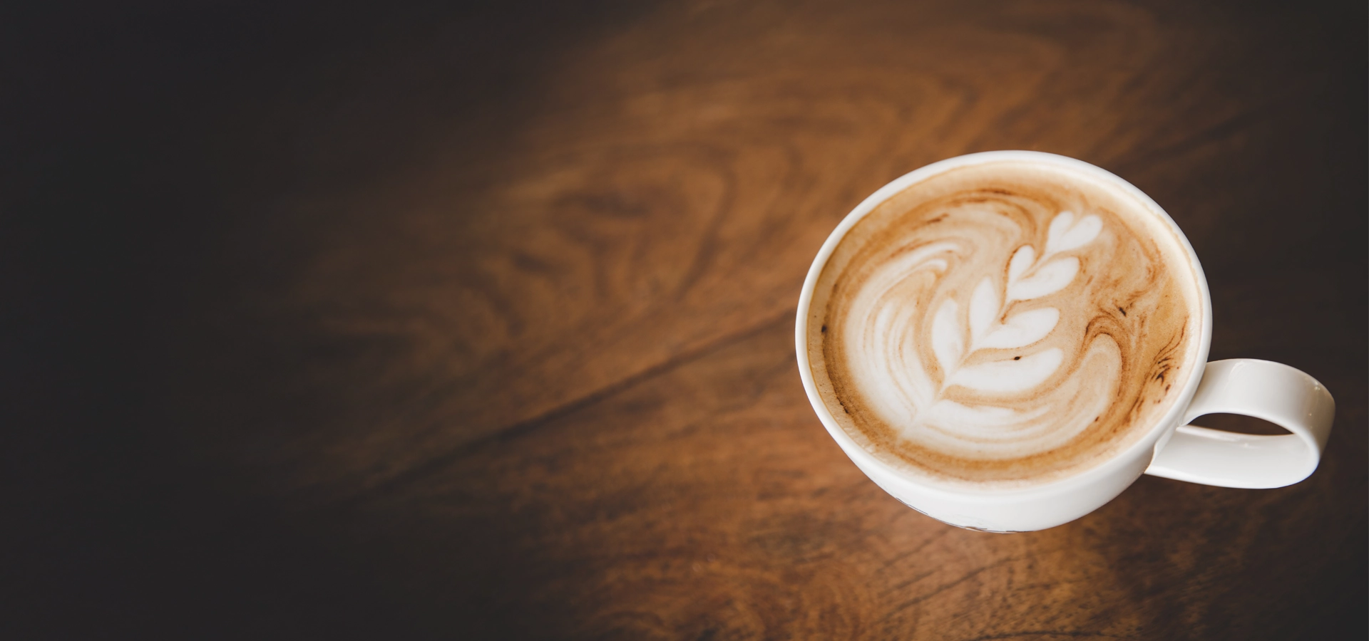 Cup of coffee with milk featuring leaf-shaped latte art, placed on a wooden table, creating a cozy coffee moment.