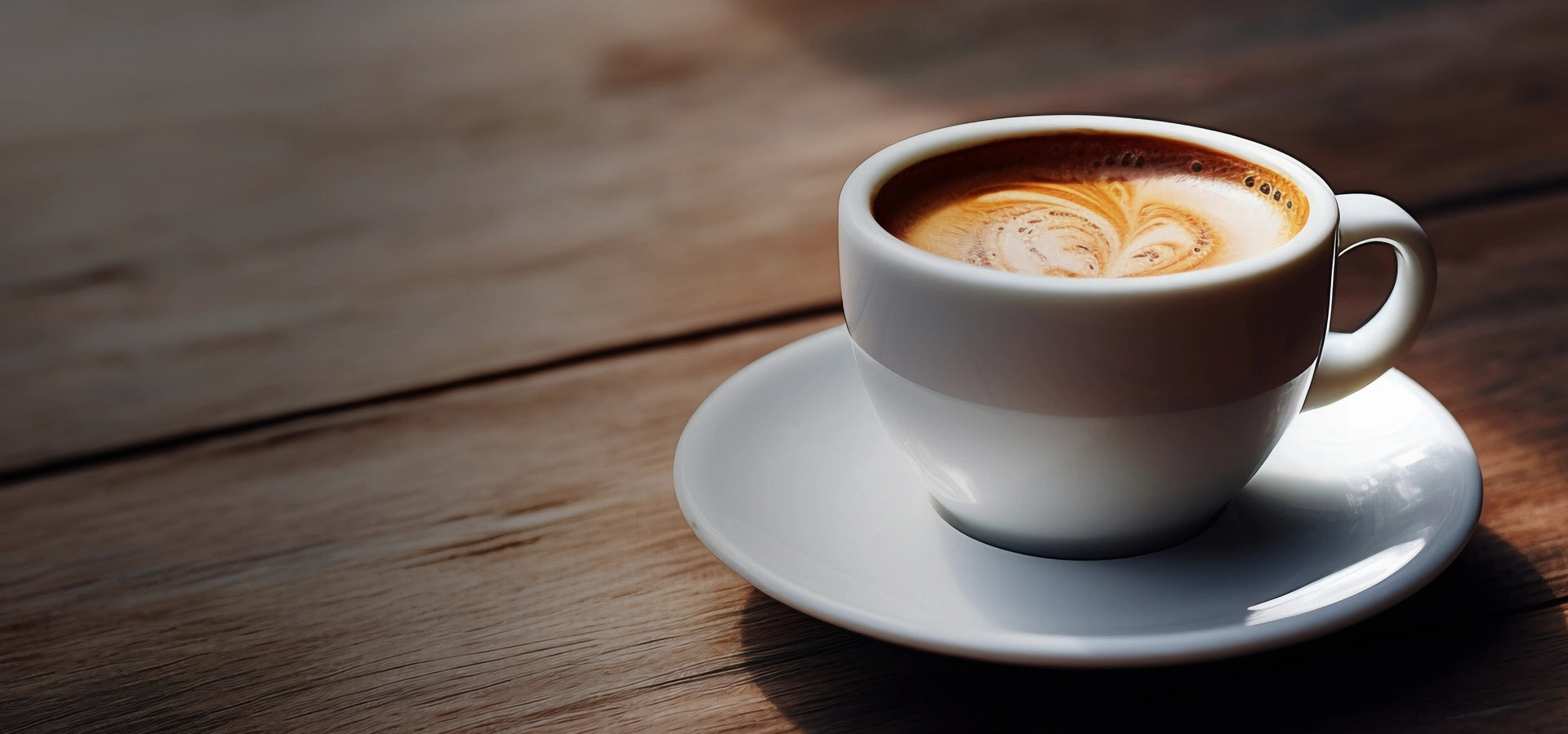 A perfectly brewed cup of coffee with latte art served in a white cup and saucer, set on a wooden table.