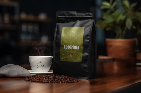 A bag of Goa Specialty Coffee Colombia Blend next to a steaming cup of coffee, with scattered coffee beans on the table, highlighting the rich flavors of coffee from the Fincas Mustafa region in Colombia.